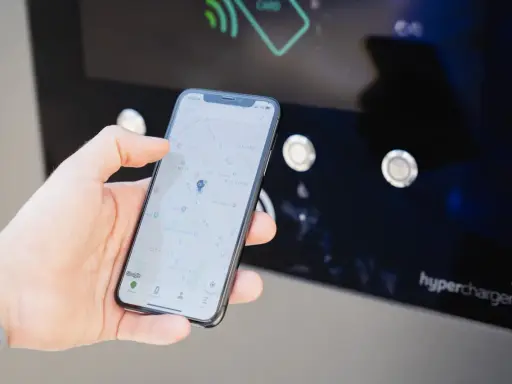 Mano che usa smartphone con mappa per trovare stazione di ricarica. L'app mostra la posizione e le opzioni per monitorare la carica.