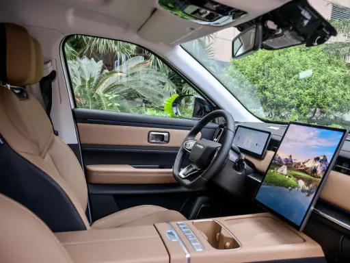 Interni del Jaecoo 7: sedili in pelle beige e nera, volante moderno e un grande schermo centrale con paesaggio montano.