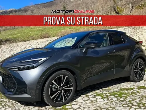 Toyota C-HR grigia parcheggiata su un selciato, con la scritta "PROVA SU STRADA". La sua linea moderna suscita un senso di delusione per chi si aspettava di più.