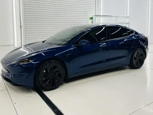 Una splendida Tesla piccola, blu scuro, con cerchi neri lucidi, parcheggiata in un garage pulito e illuminato.