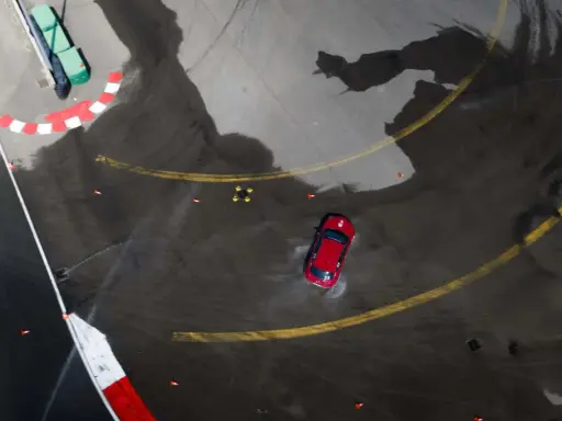 Auto rossa in derapata su asfalto bagnato, con coni arancioni e segnali di pista. I pneumatici Kumho mostrano i loro limiti in condizioni difficili.