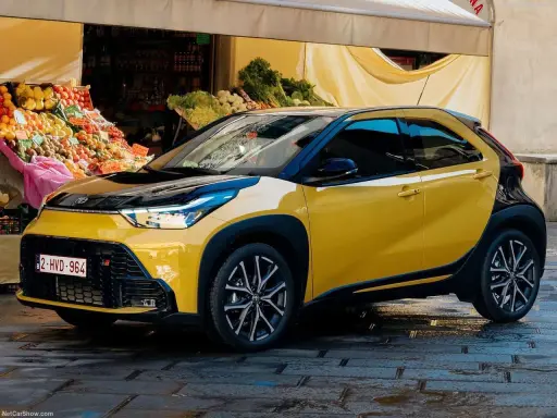 Toyota Aygo X gialla parcheggiata davanti a un mercato. Nessun problema visibile, solo un'auto elegante.