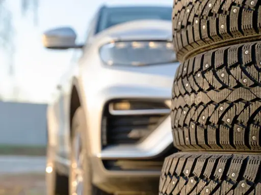 Gomme chiodate in primo piano, con un'auto bianca sfocata sullo sfondo. Mi chiedo se posso montare gomme con altezza diversa per affrontare ogni tipo di terreno.