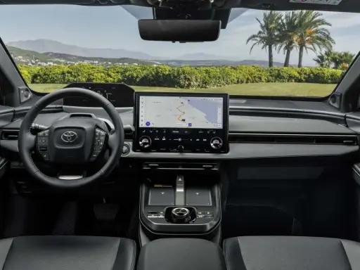 Interni moderni della Toyota bz4x con ampio display centrale e volante multifunzione. Navigazione attiva per un viaggio panoramico.
