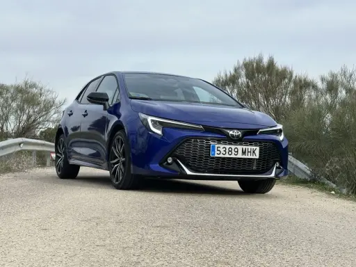 Toyota Corolla blu parcheggiata su strada sterrata, con vegetazione sullo sfondo. Un'auto che offre diverse motorizzazioni.