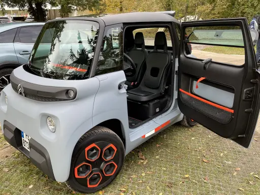 Un'auto elettrica due posti grigia con dettagli arancioni, porte aperte, sedili neri e cerchi distintivi.