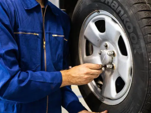 Meccanico in tuta blu controlla i bulloni di una ruota. Ci si chiede dopo quanti km si cambiano le gomme per sicurezza.