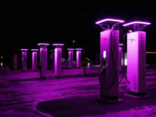 Stazione di ricarica Ionity Italia di notte, illuminata da luci viola. Colonne moderne con logo e cavi pronti per le auto elettriche.