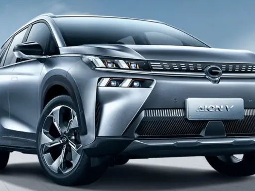 Un SUV grigio metallizzato, l'Aion V, con un design moderno e fari a LED affilati, si presenta su uno sfondo blu cielo.