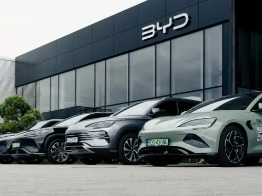 Vari modelli di auto BYD parcheggiati davanti a uno showroom moderno.