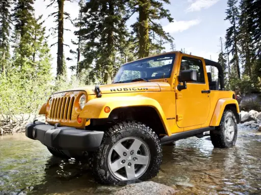 Jeep Wrangler 2.8 CRD in giallo, immerso in un ruscello tra alberi. Un'avventura che potrebbe presentare qualche problema.