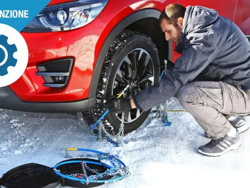 Uomo monta catene da neve su una ruota di un'auto rossa in un paesaggio innevato. Le gomme invernali sono essenziali per la sicurezza.