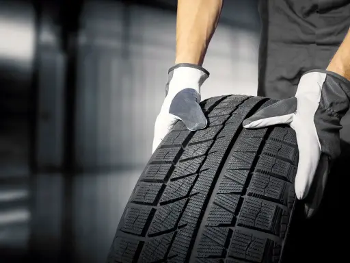 Mani guantate tengono un nuovo pneumatico. Quanto tempo ci vuole per cambiare 4 gomme? Dipende dall'officina!
