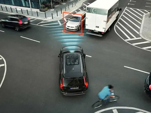 Auto rileva ciclista e attiva la forza frenante. Un'auto argentata è inquadrata, mentre un camion bianco e un'auto nera proseguono.