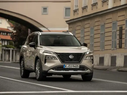 Nissan X-Trail full hybrid beige, in corsa su strada urbana con edifici storici sullo sfondo.