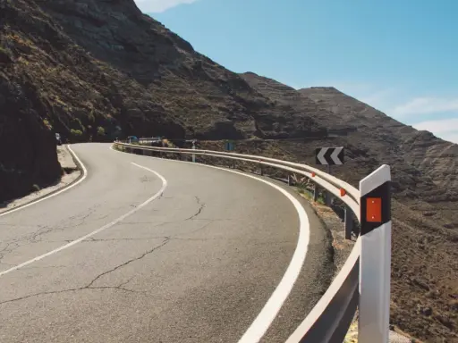 Strada tortuosa in montagna con guardrail e segnali di pericolo. I catadiottri cosa sono? Sono quei dispositivi che riflettono la luce per segnalare la strada.