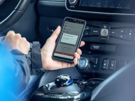 Mano che tiene uno smartphone con app di navigazione attiva, mostrando il **power cruise control** per un viaggio in auto.