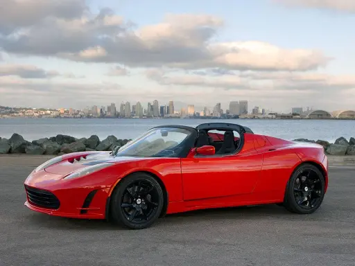 Tesla Roadster rosso fiammante, con la silhouette di una città all'orizzonte.