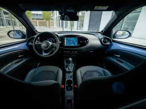 Interni moderni della Toyota Aygo X: volante, cruscotto con navigatore e sedili in tessuto.