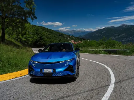 L'Alpine A290 sfreccia su una strada di montagna panoramica, con un cielo azzurro e montagne sullo sfondo.
