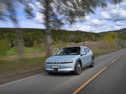 La Hyundai Ioniq 5 sfreccia su una strada panoramica tra alberi e colline verdi, con un cielo nuvoloso.