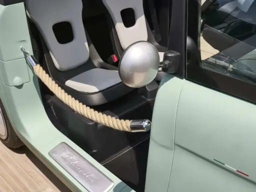 Interni Fiat Topolino: sedili chiari, corda decorativa e logo "Dolcevita" sulla soglia.