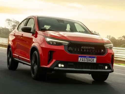 La Fiat Fastback 2026 rossa sfreccia su una pista, con il sole che illumina il cielo.