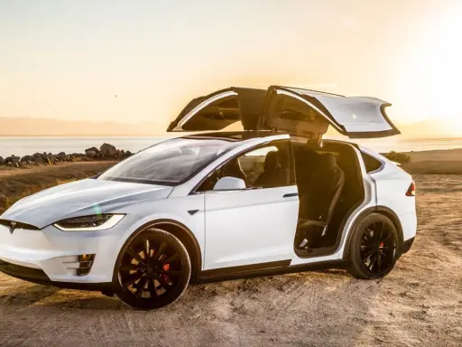 Tesla Model X bianca con portiere ad ali di gabbiano aperte al tramonto, un'auto elettrica che rappresenta il lusso e l'innovazione, forse la tesla più costosa.