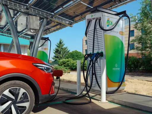 Un'auto rossa si ricarica presso colonnine ultra fast sotto pannelli solari.