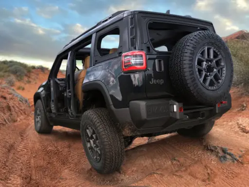 Un fuoristrada elettrico Jeep nero affronta un sentiero sterrato nel deserto, con le portiere aperte e una ruota di scorta sul retro.