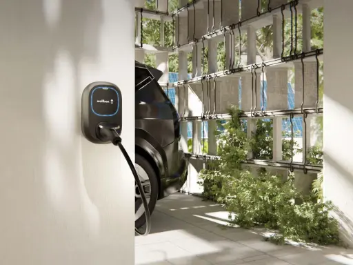 Wallbox per auto elettriche, con cavo collegato a un'auto scura. L'ambiente è moderno, con elementi verdi e pannelli solari visibili.