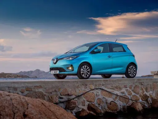 Un'elegante Renault Zoe blu, uno dei tanti modelli Renault, è parcheggiata su un muretto di pietra con il mare e le montagne sullo sfondo.