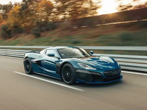 La **auto elettrica più veloce** sfreccia su una strada, con il sole che tramonta tra gli alberi sullo sfondo.