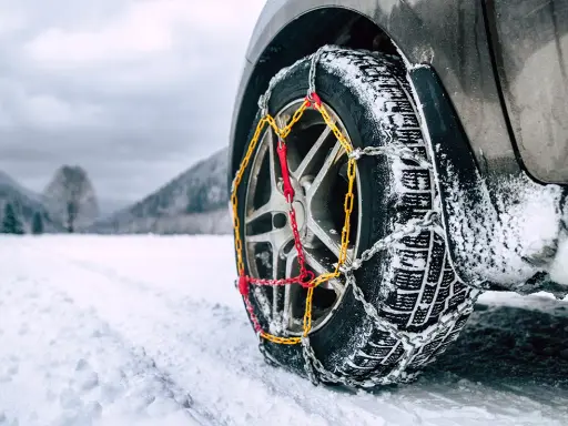 Catene da neve senza codice: come riconoscerle. Ruota di un'auto con catene montate su strada innevata.