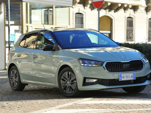 A light green Skoda Fabia hatchback with a black roof is parked on a cobblestone street in front of a building.