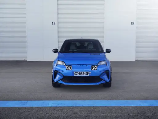 La nuova Alpine A290, un'auto elettrica sportiva blu brillante, attende il suo momento davanti a un garage con porte chiuse.