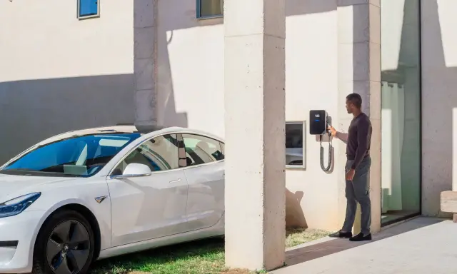 Uomo accanto a un'auto elettrica bianca, che interagisce con una wallbox V2C. Un bonus per la ricarica intelligente.