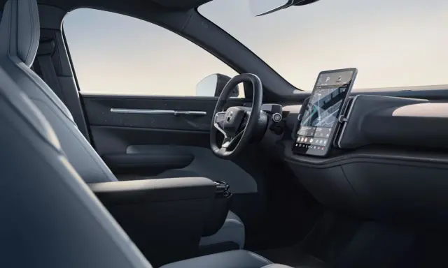 Interni minimalisti del Volvo EX30: sedili chiari, volante moderno e grande schermo centrale con navigazione.