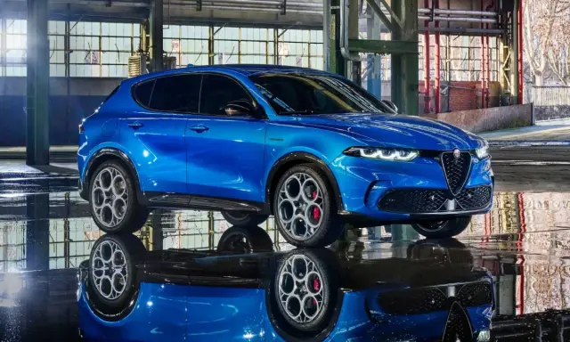 Alfa Romeo Tonale blu, un esempio di stellantis auto elettriche, riflette sul pavimento bagnato di un capannone industriale.