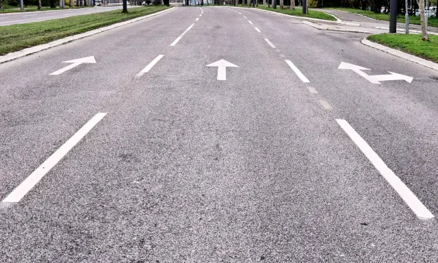 Strada con frecce bianche che indicano le corsie di canalizzazione.