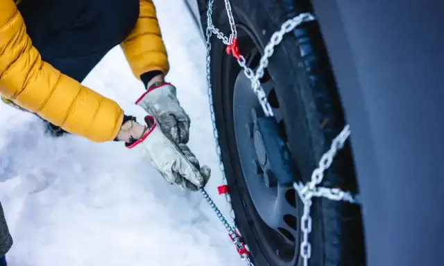 Mani guantate montano le catene da neve su una gomma 4 stagioni. Se ho le gomme 4 stagioni devo avere le catene per la sicurezza invernale.