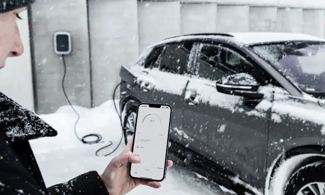 Persona controlla la carica di auto elettriche con lo smartphone, mentre nevica. Il freddo non ferma la tecnologia.