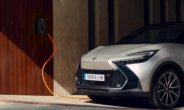 Toyota C-HR GR in argento, con cavo arancione collegato alla stazione di ricarica. L'auto plug-in è pronta per la sua prossima avventura.