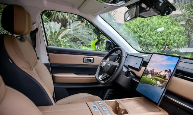 Interni del Jaecoo 7: sedili in pelle beige e nera, volante moderno e un grande schermo centrale con paesaggio montano.