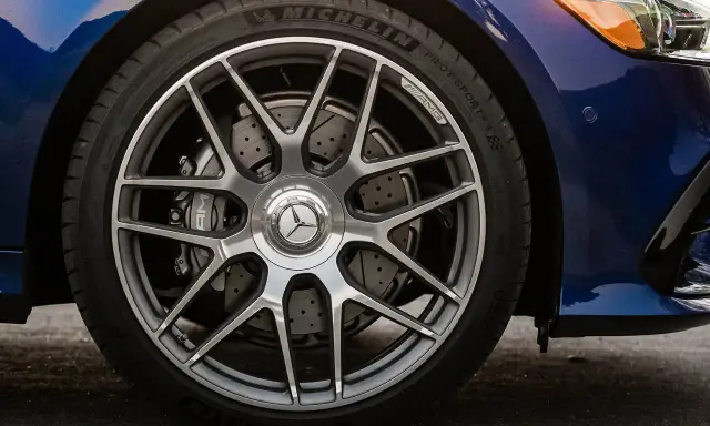 Ruota di un'auto blu con cerchi AMG e freni a disco forati. Il pneumatico Michelin mostra un leggero segno di usura.