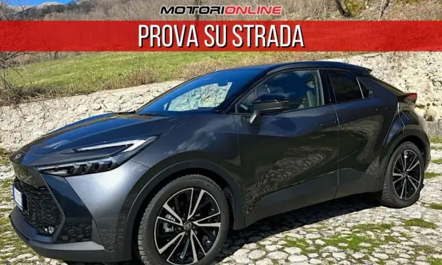 Toyota C-HR grigia parcheggiata su un selciato, con la scritta "PROVA SU STRADA". La sua linea moderna suscita un senso di delusione per chi si aspettava di più.
