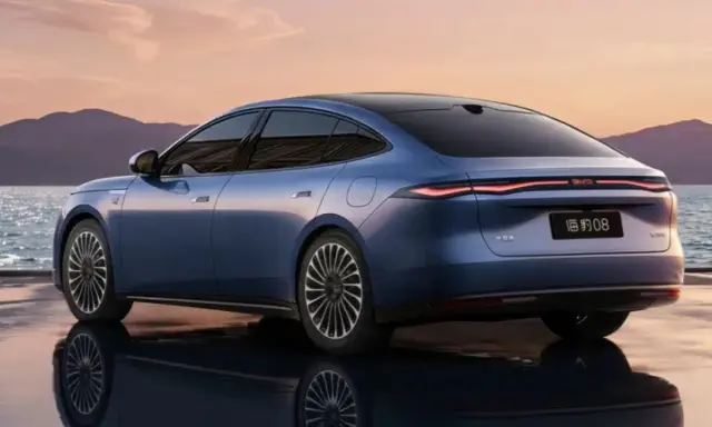 BYD Seal 08, berlina blu elettrica, riflette sull'acqua al tramonto, con montagne sullo sfondo.