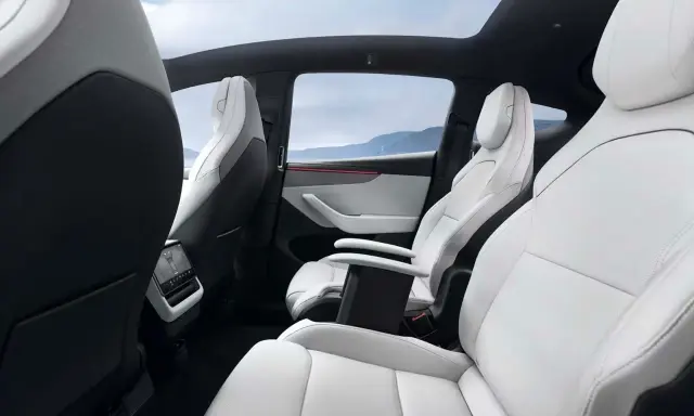Interni bianchi e neri del Tesla Model Y, con sedili in pelle, tetto panoramico e vista sulle montagne.