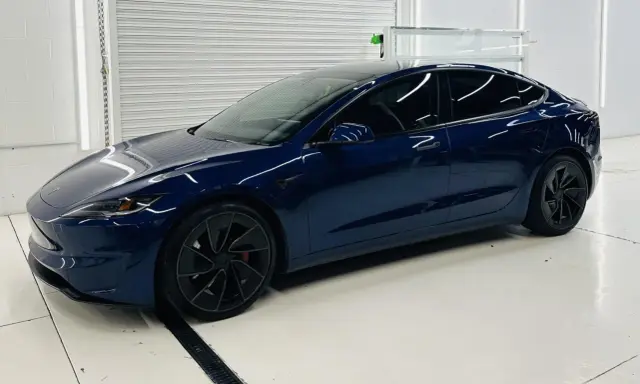Una splendida Tesla piccola, blu scuro, con cerchi neri lucidi, parcheggiata in un garage pulito e illuminato.