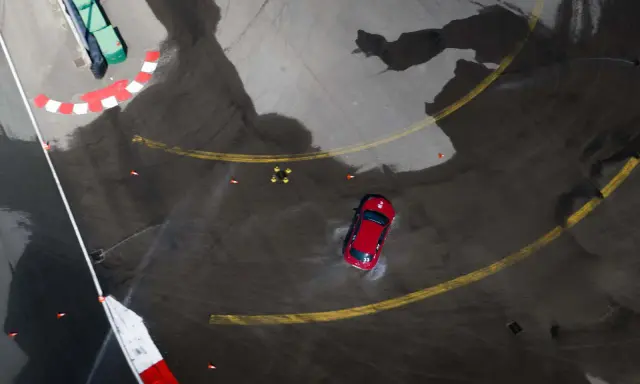 Auto rossa in derapata su asfalto bagnato, con coni arancioni e segnali di pista. I pneumatici Kumho mostrano i loro limiti in condizioni difficili.